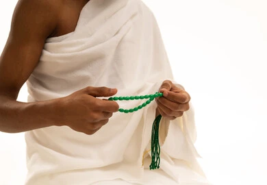 العبادة والطاعة والتقرب الى الله, التسبيح والتهليل وذكرالله، أداء مناسك الحج والعمرة، بورتريه مقرب ليد شاب عربي خليجي سعودى يرتدي ثياب الإحرام يسبح بالسبحة الخضراء، خلفية بيضاء