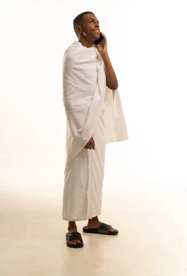 Making a phone call via a mobile phone, a portrait of a young Arab Gulf Saudi man wearing Ihram clothing making a phone call via his mobile, visiting the Sacred House of God in Mecca, full-body image, white background.