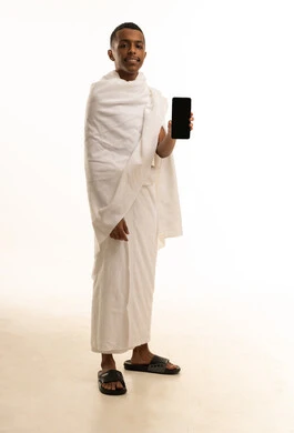 A portrait of a young Saudi Arabian Gulf man wearing Ihram clothing, holding a mobile phone with a blank black screen, visiting the Holy House of God in Mecca, full-body image, white background. A portrait of a young Saudi Arabian Gulf man wearing Ihram clothing, holding a mobile phone with a blank black screen, visiting the Holy House of God in Mecca, full-body image, white background.