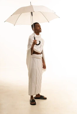 بورتريه لشاب عربي خليجي سعودى يرتدي ثياب الإحرام يحمل بيده مظلة شمسية للحماية والتظلل،  زيارة المشاعر المقدسة في مكة المكرمة، تعابير السرور الاستعداد لأداء فريضة الحج، الجسم بالطول الكامل، خلفية بيضاء