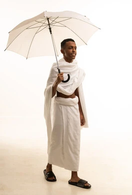 زيارة المشاعر المقدسة في مكة المكرمة، بورتريه لشاب عربي خليجي سعودى يرتدي ثياب الإحرام  يحمل بيده مظلة شمسية للحماية والتظلل، تعابيرالسروربالاستعداد لأداء فريضة الحج، الجسم بالطول الكامل، خلفية بيضاء