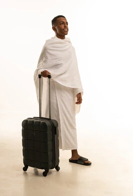 العبادة والتقرب الى الله، التجهيز و الاستعداد للسفر والذهاب لأداء العمرة في مكة المكرمة، بورتريه لشاب عربي خليجي سعودى يرتدي ثياب الإحرام ويمسك بيده حقيبة السفر، الجسم بالطول الكامل، خلفية بيضاء