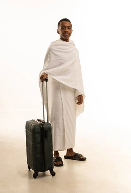 Preparation and readiness for travel and going to perform Umrah in Mecca, a portrait of a young Arab Gulf Saudi man wearing Ihram clothing and holding a travel bag in his hand, heading and setting off to visit the Sacred House of God, full-body shot, white background.