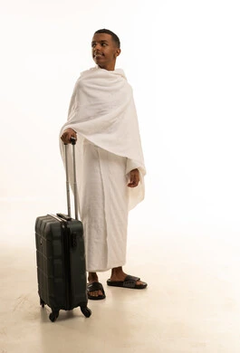 ايماءات السعادة والحماس للوصول لمكة المكرمة، بورتريه لشاب عربي خليجي سعودى يرتدي ثياب الإحرام ويمسك بيده حقيبة السفر، الاستعداد للتوجه والانطلاق لزيارة بيت الله الحرام، الذهاب لأداء فريضة الحج والعمرة، الجسم بالطول الكامل، خلفية بيضاء