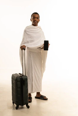 الذهاب لأداء فريضة الحج والعمرة، الاستعداد للتوجه والانطلاق لزيارة بيت الله الحرام، بورتريه لشاب عربي خليجي سعودى يرتدي ثياب الإحرام ويمسك بيده حقيبة السفرويحمل بيده الهاتف ويقوم بعرض شاشة سوداء فارغة عبر الهاتف المحمول، الجسم بالطول الكامل، خلفية بيضاء