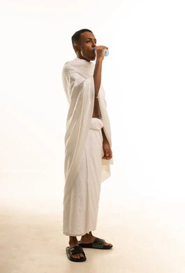 الارتواء بماء زمزم، أداء مناسك الحج والعمرة، بورتريه لشاب عربي خليجي سعودى يرتدي ثياب الإحرام يحمل يقوم بشرب المياة العذبة، صورة الجسم بالطول الكامل، خلفية بيضاء