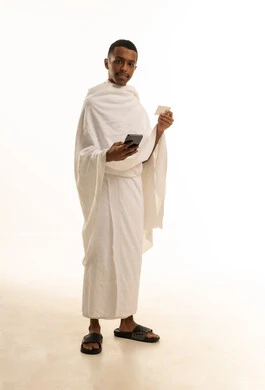 الاستعداد للذهاب للحج، بورتريه لشاب عربي خليجي سعودى يرتدي ثياب الإحرام  يحمل بيده الهاتف المحمول و تذكرة السفر، صورة الجسم بالطول الكامل، خلفية بيضاء