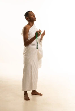 بورتريه من الجانب لشاب عربي خليجي سعودى يرتدي ثياب الإحرام يرفع يديه للأعلى يدعو بتضرع وخشوع، الدعاء والتقرب إلى الله، مفهوم أركان الإسلام، أداء مناسك الحج والعمرة، خلفية بيضاء