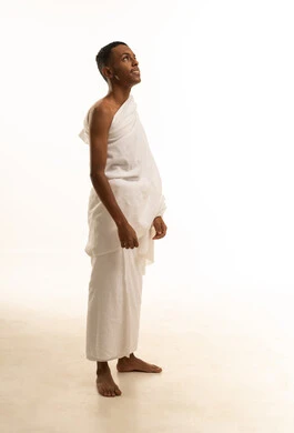 A side portrait of a smiling Arab Gulf Saudi Muslim man wearing Ihram clothing, performing the rituals of Hajj and Umrah, the concept of the pillars of Islam, looking up, with a white background.