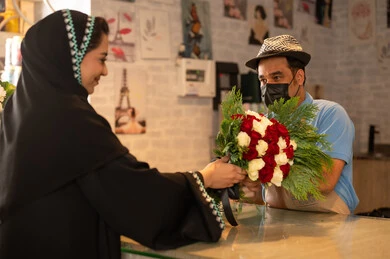 Gestures indicating joy and happiness, shops and stores selling natural flowers and roses for holidays and occasions, a Gulf Arab Saudi woman wearing an abaya and hijab is buying a bouquet of natural red roses from the seller, gestures indicating joy and happiness.