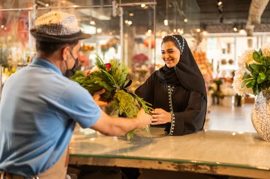 Stores and shops selling natural flowers and bouquets for holidays and occasions, a Gulf Arab Saudi woman wearing an abaya and hijab is buying a bouquet of natural red flowers from the seller, gestures indicating joy and happiness.
