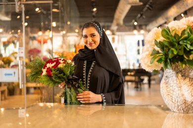 A Saudi Arabian Gulf woman wearing an abaya and hijab holds a bouquet of natural red roses with gestures of joy and happiness, buying flowers and natural blooms for holidays and occasions from shops and stores. A Saudi Arabian Gulf woman wearing an abaya and hijab holds a bouquet of natural red roses with gestures of joy and happiness, buying flowers and natural blooms for holidays and occasions from shops and stores.