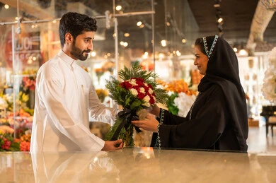 A happy Saudi Arabian Gulf couple is celebrating Valentine's Day, the husband is giving his wife a bouquet of flowers, the wife expresses surprise and joy through her facial and hand gestures, Valentine's Day, happy holidays and occasions, celebrating Christmas, background of a flower shop.