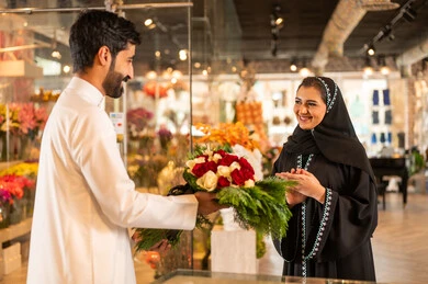 Celebrating Christmas, a happy Saudi Arabian Gulf couple celebrating Valentine's Day, the husband presents his wife with a bouquet of flowers, the wife expresses with facial and hand gestures indicating surprise and joy, Valentine's Day, happy holidays and occasions, background of a flower shop.