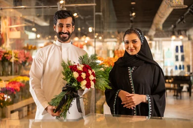 A happy Saudi Arabian Gulf couple is celebrating Valentine's Day, the husband is giving his wife a bouquet of flowers, the wife expresses surprise and joy through her facial and hand gestures, Valentine's Day, happy holidays and occasions, celebrating Christmas, background of a flower shop.