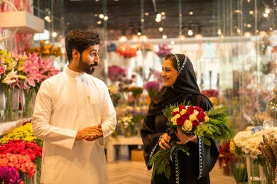 A happy Saudi Arabian Gulf couple is celebrating Valentine's Day, the husband is giving his wife a bouquet of flowers, the wife expresses surprise and joy through her facial and hand gestures, Valentine's Day, happy holidays and occasions, celebrating Christmas, background of a flower shop.