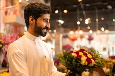 مفهوم الود والالفه،  زوجان عربيان خليجيان سعوديان سعيدان يحتفلان بعيد الحب , الزوج يقدم لزوجته باقة ورد ,، يوم عيد الفلانتاين , أعياد ومناسبات سعيده , الاحتفال بعيد الميلاد , خلفية محل بيع الورود.