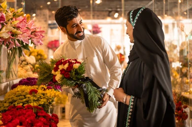 The husband presents his wife with a bouquet of flowers, a happy Saudi Arabian couple celebrating Valentine's Day, the wife expresses with facial and hand gestures indicating surprise and joy, Valentine's Day, happy holidays and occasions, celebrating Christmas, background of a flower shop.