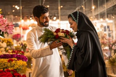 Celebrating Christmas, a happy Saudi Arabian Gulf couple celebrating Valentine's Day, the husband presents his wife with a bouquet of flowers, the wife expresses with facial and hand gestures indicating surprise and joy, Valentine's Day, happy holidays and occasions, background of a flower shop.