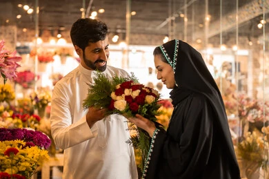 الاحتفال بالأعياد والمناسبات الخاصة ، زوج عربي خليجي سعودي يرتدي الثوب الابيض يقوم بإهداء باقة ورد احمر طبيعي لزوجته، تعابير وايماءات المودة والسعاده، محلات ومتاجر بيع وشراء الورود والزهور الطبيعية