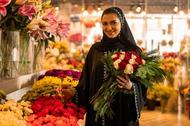 محلات ومتاجر بيع الورد, شراء الورود والزهور الطبيعية ، امرأة عربية خليجية سعودية ترتدي العباءة والحجاب تحمل باقة ورد احمر طبيعي بايماءات الفرح والسعاده