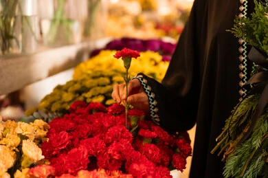 شراء الورود والزهور الطبيعية للأعياد والمناسبات من المحلات والمتاجر, امرأة عربية خليجية سعودية ترتدي العباءة والحجاب تحمل باقة ورد احمر طبيعي بايماءات الفرح والسعاده