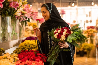 Buying natural flowers and roses for holidays and occasions from shops and stores, an Arab Gulf Saudi woman wearing an abaya and hijab holding a bouquet of natural red roses with gestures of joy and happiness. Buying natural flowers and roses for holidays and occasions from shops and stores, an Arab Gulf Saudi woman wearing an abaya and hijab holding a bouquet of natural red roses with gestures of joy and happiness.
