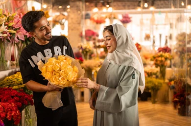 ايماءات الفرح والسعاده ، امرأة عربية خليجية سعودية ترتدي العباءة والحجاب تحمل باقة ورد احمر طبيعي, شراء الورود والزهور الطبيعية للأعياد والمناسبات من المحلات والمتاجر