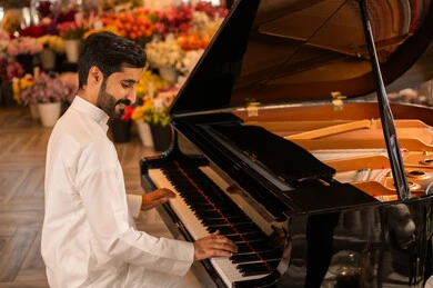 مفهوم الفن والموسيقي ،تقديم البرامج والفنون الموسيقية والفن المسرحي، قضاء الوقت بالعزف على الألات الوترية، الطرب والانشطة ترفيهية، رجل خليجي سعودي عربي فنان يرتدي الثوب الابيض يجلس امام آلة البيانو الموسيقية ويستمتع بالعزف