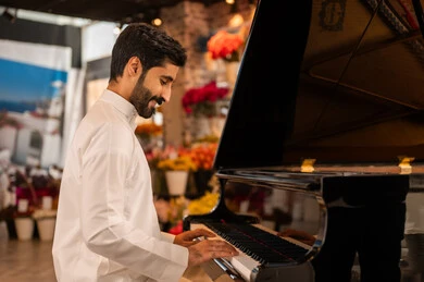 مواهب فنية موسيقية، قضاء الوقت بالعزف على الألات الوترية، الطرب والانشطة ترفيهية، تقديم البرامج والفنون الموسيقية والفن المسرحي، رجل خليجي سعودي عربي فنان يرتدي الثوب الابيض يجلس امام آلة البيانو الموسيقية ويستمتع بالعزف