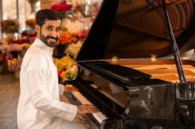 مفهوم الفن والموسيقي ،تقديم البرامج والفنون الموسيقية والفن المسرحي، قضاء الوقت بالعزف على الألات الوترية، الطرب والانشطة ترفيهية، رجل خليجي سعودي عربي فنان يرتدي الثوب الابيض يجلس امام آلة البيانو الموسيقية ويستمتع بالعزف