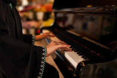Musical artistic talents, spending time playing string instruments, singing and recreational activities, presenting programs and musical arts and theatrical art, an Arab Gulf Saudi woman artist wearing an abaya and hijab sitting in front of a musical piano and enjoying playing.