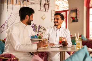 Expressions of joy and happiness, spending enjoyable times with friends, discussion and dialogue in calm atmospheres, sharing cold drinks, two Arab Gulf friends from Saudi Arabia wearing white thobes sitting in one of the upscale cafes.