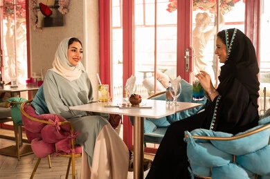 النقاش والحوار في الأجواء الهادئة، كوفي شوب راقي بالمملكة العربية السعودية، تعابير السعادة والسرور ،قضاء أوقات ممتعة مع الأصدقاء، مشاركة المشروبات الباردة ، صديقتان عربيتان خليجيتان سعوديتان ترتديان العباءة والحجاب تجلسان  في إحدى المقاهي الراقية