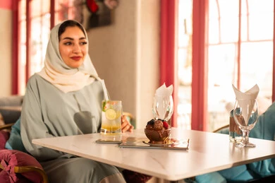 قضاء أوقات ممتعة مع الأصدقاء، كوفي شوب راقي بالمملكة العربية السعودية، تعابير السعادة والسرور ،النقاش والحوار في الأجواء الهادئة، مشاركة المشروبات الباردة ، صديقتان عربيتان خليجيتان سعوديتان ترتديان العباءة والحجاب تجلسان  في إحدى المقاهي الراقية