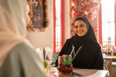 النقاش والحوار في الأجواء الهادئة، كوفي شوب راقي بالمملكة العربية السعودية، تعابير السعادة والسرور ،قضاء أوقات ممتعة مع الأصدقاء، مشاركة المشروبات الباردة ، صديقتان عربيتان خليجيتان سعوديتان ترتديان العباءة والحجاب تجلسان  في إحدى المقاهي الراقية