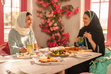Expressions of joy and happiness, a dining table filled with a variety of delicious dishes and appetizers, gestures of happiness while spending enjoyable times with friends, a gathering of friends at a delicious breakfast table, a close-up image of a lunch invitation for Saudi Gulf Arab friends enjoying food at a luxury restaurant.
