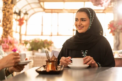 كوفي شوب راقي بالمملكة العربية السعودية، مشاركة المشروبات الساخنة مع الاصدقاء ، تعابير السعادة والسرور بلمة الرفاق، تطوير العلاقات الإجتماعية، قضاء وقت ممتع مع الأصدقاء، الاستمتاع بالاجواء السعيده ، صديقتان عربيتان خليجيتان سعوديتان تجلسان على طاولة في المقهى