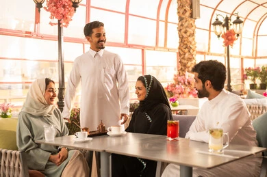 Enjoying hot drinks, a classy coffee shop in the Kingdom of Saudi Arabia, expressions of happiness and joy with friends, developing social relationships, spending enjoyable time with friends, enjoying the happy atmosphere, a group of Arab Gulf Saudi friends sitting at a table in the café.