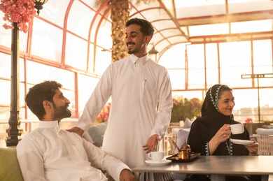 Developing social relationships, an upscale coffee shop in the Kingdom of Saudi Arabia, expressions of happiness and joy with friends, spending enjoyable time with friends, enjoying hot beverages, enjoying the happy atmosphere, a group of Arab Gulf Saudi friends sitting at a table in the café.