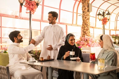 كوفي شوب راقي بالمملكة العربية السعودية، تعابير السعادة والسرور بلمة الرفاق، تطوير العلاقات الإجتماعية، قضاء وقت ممتع مع الأصدقاء، الاستمتاع بالمشروبات الساخنه ، الاستمتاع بالاجواء السعيده ، مجموعة اصدقاء عرب خليجيين سعوديين يجلسون على طاولة في المقهى