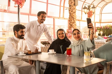 توثيق اللحظات السعيدة ، التقاط صور تذكارية بواسطة الجوال ،كوفي شوب راقي بالمملكة العربية السعودية، تعابير السعادة والسرور بلمة الرفاق، تطوير العلاقات الإجتماعية، قضاء وقت ممتع مع الأصدقاء، الاستمتاع بالمشروبات الساخنه ، الاستمتاع بالاجواء السعيده ، مجموعة اصدقاء عرب خليجيين سعوديين يجلسون على طاولة في المقهى