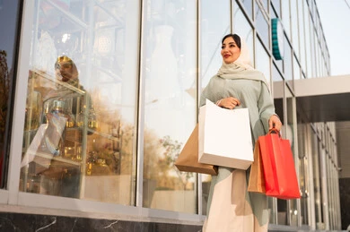 A Gulf Arab Saudi woman wearing an abaya and hijab is looking at something during the day, feeling pride and honor in the architectural progress, growth, and urban development in Saudi Arabia, with gestures of joy and happiness, strolling and breathing in the fresh air outside.