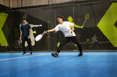 التدرب على إتقان لعبة البادل، رياضات شبابية وأنشطة ترفيهية، القيام بتمرينات رياضة التنس، خوض المباريات والبطولات بتحدي وعزيمة، شاب عربي خليجي سعودي يرتدي ملابس رياضية يلعب مباراة كرة المضرب برفقة زميلة، تعابير وإيماءات تدل على الحماس والاندماج بالتمرين