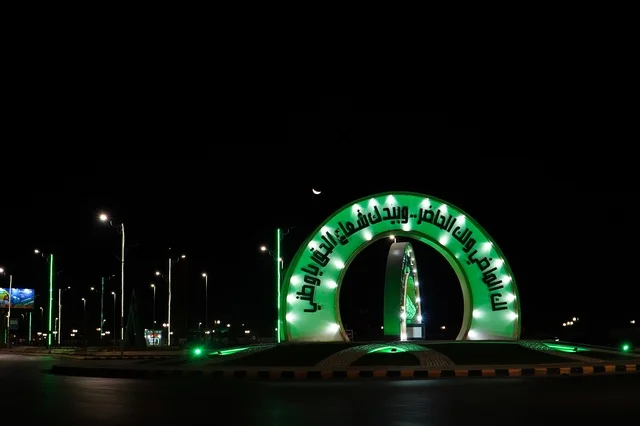 The square of the province of Turaif, a sculpture with the phrase "You have the past and you have the present, and in your hand is the ray of truth, O my homeland." Places and areas in Riyadh, love for the homeland and belonging to it, pride in national identity, the Kingdom of Saudi Arabia, a lit roundabout at night.