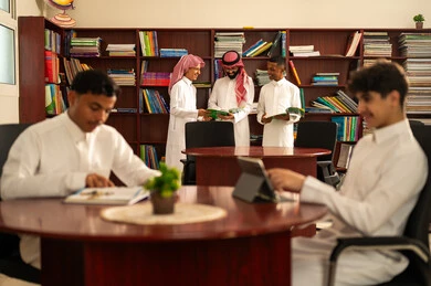 The evolution of teaching methods, the love of learning and exploring ideas, developed curricula and e-learning, benefiting from modern technologies and technology in learning and studying, a group of Arab Gulf Saudi students wearing white thobes sitting inside the school library with their teacher, using a tablet, doing homework. The evolution of teaching methods, the love of learning and exploring ideas, developed curricula and e-learning, benefiting from modern technologies and technology in learning and studying, a group of Arab Gulf Saudi students wearing white thobes sitting inside the school library with their teacher, using a tablet, doing homework.