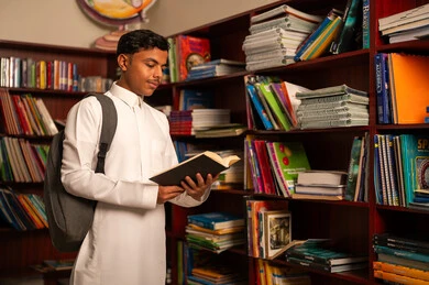 مدارس أكاديميه في المملكة العربية السعودية، بيئه مدرسيه تعليميه متطوره، مفهوم القراءه والثقافه، الاستمتاع بقراءة الكتب، طالب عربي سعودي خليجي يقوم بقراءة كتاب من المكتبة المدرسية