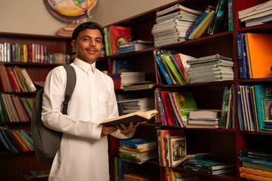بيئه مدرسيه تعليميه متطوره، مفهوم القراءه والثقافه، الاستمتاع بقراءة الكتب، طالب عربي سعودي خليجي يقوم بقراءة كتاب من المكتبة المدرسية, مدارس أكاديميه في المملكة العربية السعودية