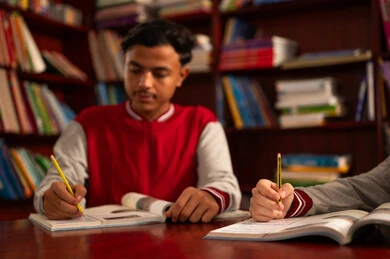 Gestures of integration and focus, diligence and hard work to achieve success and excellence, completing school assignments, returning to school, an Arab Gulf Saudi student wearing a school uniform sitting inside the school library reading a book.