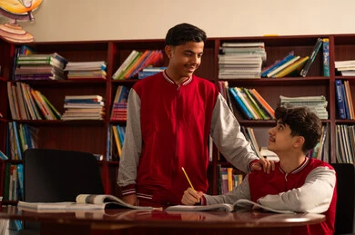 التعاون الدراسي والمشاركة في حل التمارين والواجبات، التعليم في المملكة العربية السعودية، طالبان عربيان خليجيان سعوديان يجلسان في المكتبة المدرسية، الاستمتاع بقراءة الكتب المدرسية، تأدية الواجبات المدرسية